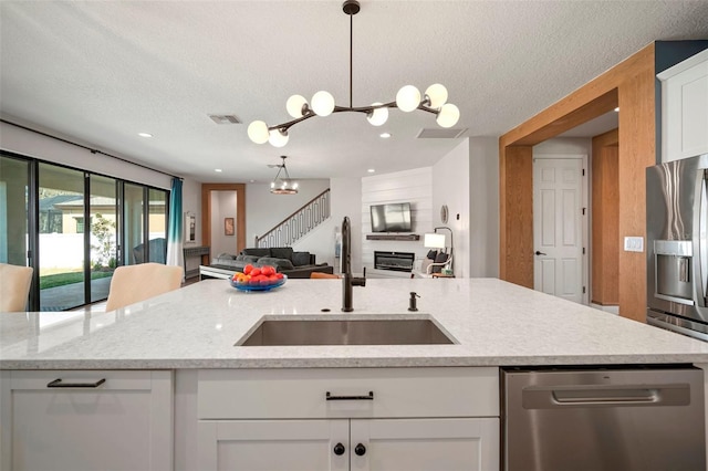 kitchen with white cabinets, a glass covered fireplace, appliances with stainless steel finishes, open floor plan, and a sink