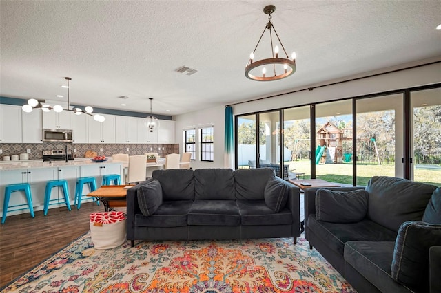 living area with a chandelier, visible vents, dark wood finished floors, and a textured ceiling