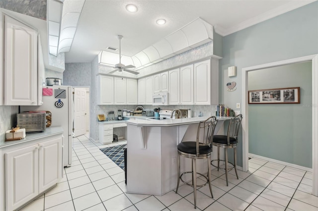 kitchen featuring ceiling fan, white microwave, a breakfast bar area, visible vents, and white cabinets