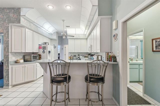 kitchen featuring a peninsula, white refrigerator with ice dispenser, a skylight, white cabinets, and a kitchen bar