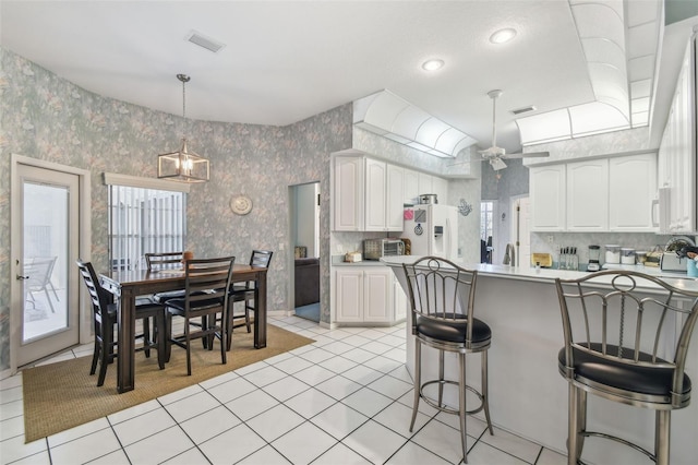 kitchen with light tile patterned floors, white refrigerator with ice dispenser, a breakfast bar, visible vents, and wallpapered walls