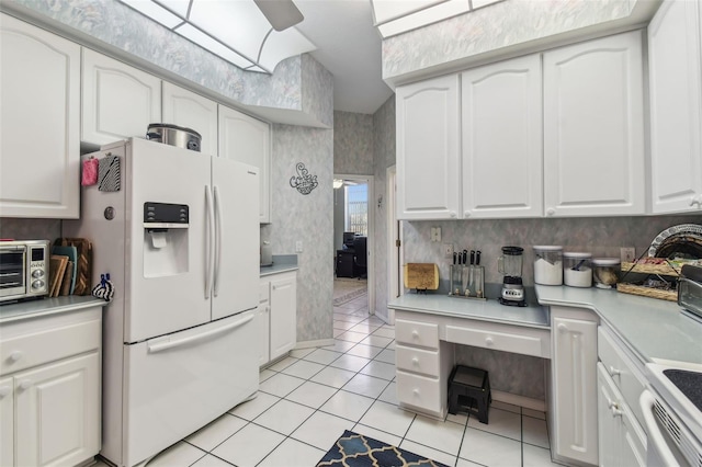 kitchen featuring light countertops, white refrigerator with ice dispenser, white cabinets, and wallpapered walls