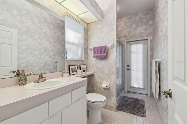 bathroom with vanity, a shower stall, toilet, and wallpapered walls