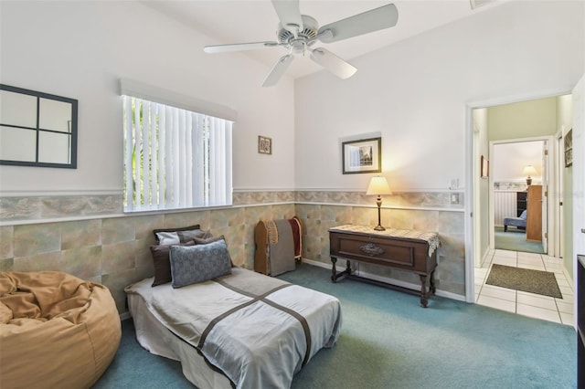 carpeted bedroom with a wainscoted wall, a ceiling fan, and tile patterned floors