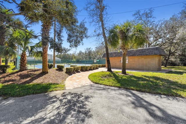 view of community featuring a tennis court, fence, and a yard