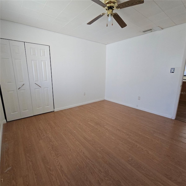 unfurnished bedroom with baseboards, visible vents, ceiling fan, wood finished floors, and a closet