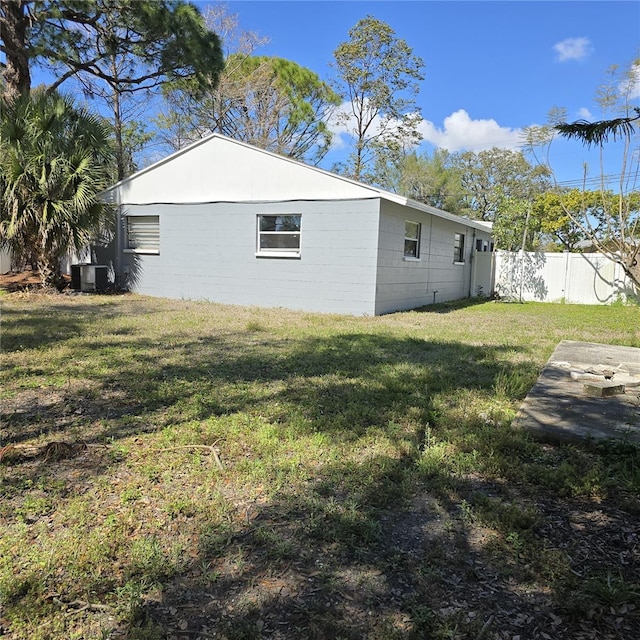 view of side of home with a yard, concrete block siding, fence, and central air condition unit