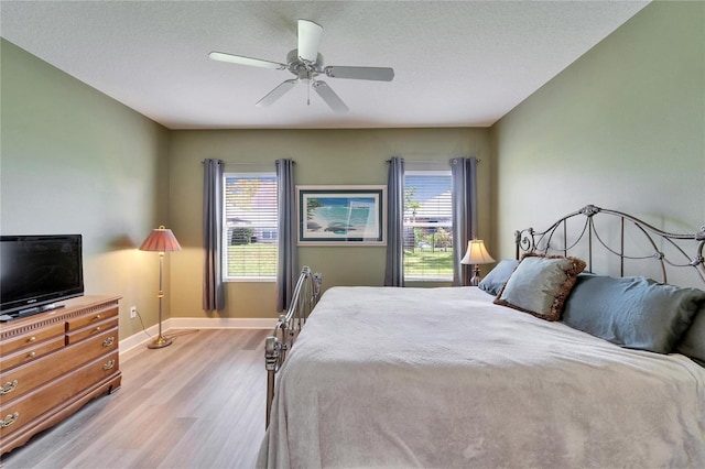 bedroom featuring ceiling fan, light wood-style flooring, baseboards, and a textured ceiling