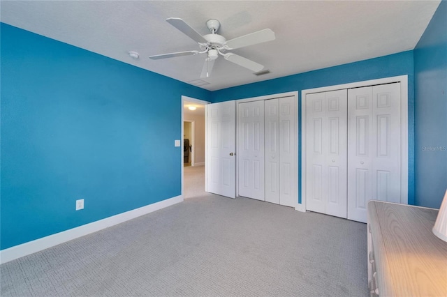 unfurnished bedroom with carpet, two closets, visible vents, a ceiling fan, and baseboards