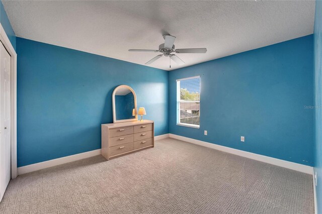 unfurnished bedroom with a textured ceiling, carpet floors, a ceiling fan, baseboards, and a closet