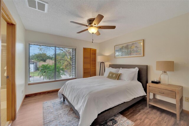 bedroom with a textured ceiling, wood finished floors, visible vents, and a ceiling fan