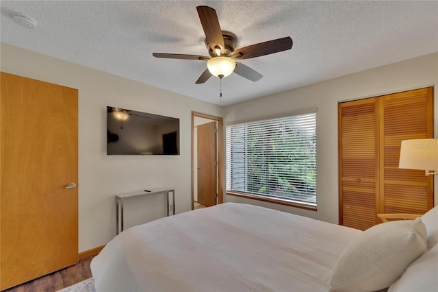 bedroom featuring a textured ceiling, wood finished floors, a ceiling fan, baseboards, and a closet