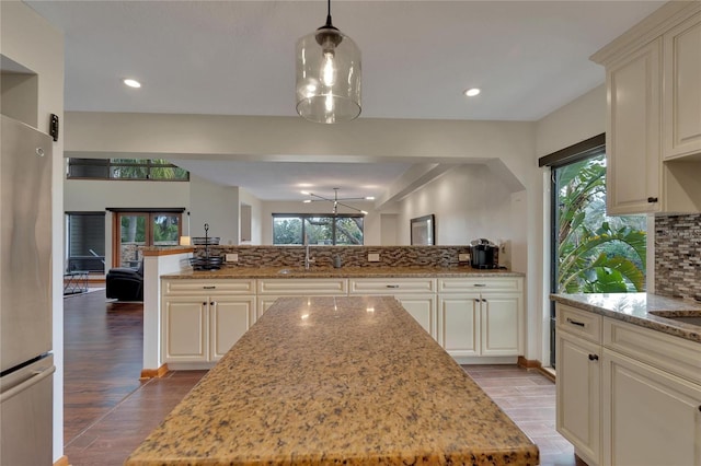 kitchen with recessed lighting, wood finished floors, backsplash, freestanding refrigerator, and light stone countertops