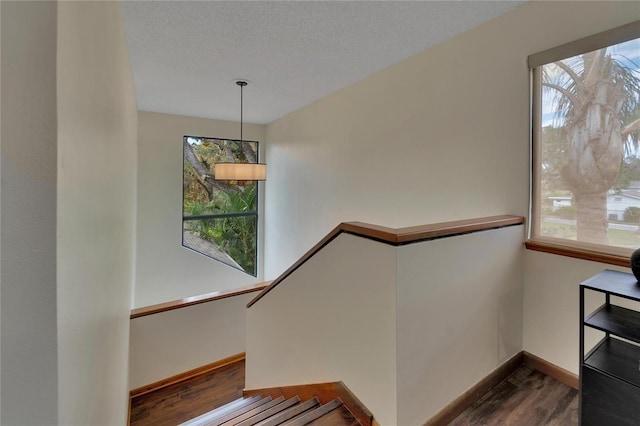 staircase with a textured ceiling, wood finished floors, and baseboards