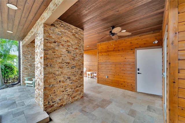 unfurnished room with a ceiling fan, wood walls, wood ceiling, and stone tile floors