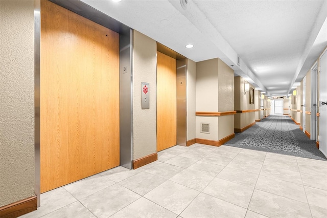 hall with elevator, a textured wall, baseboards, and tile patterned floors