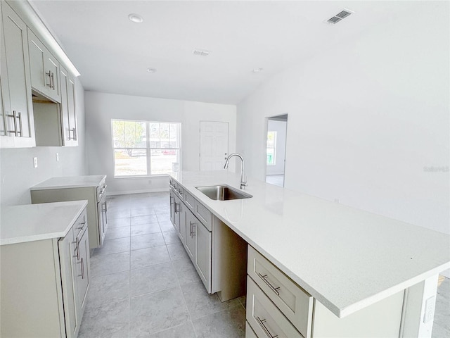 kitchen featuring light tile patterned floors, light countertops, visible vents, a sink, and an island with sink