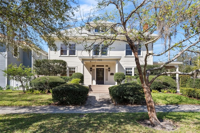 american foursquare style home featuring a front yard and a chimney