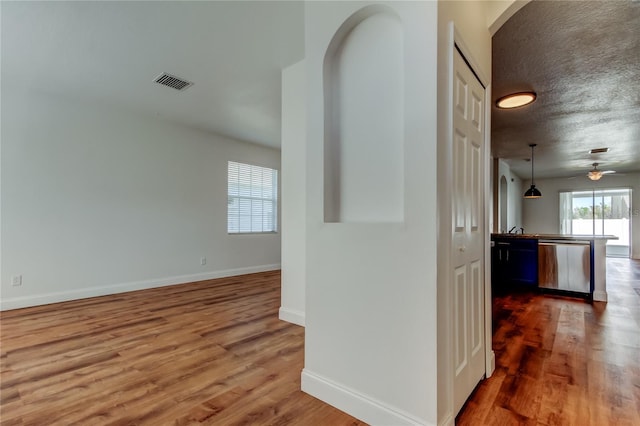 hallway featuring arched walkways, visible vents, baseboards, and wood finished floors