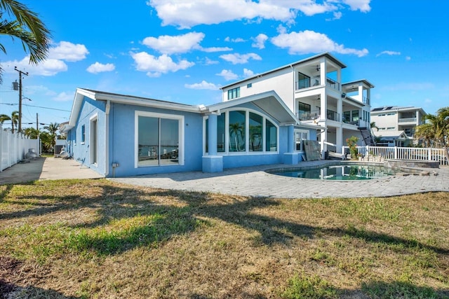 rear view of house featuring a balcony, fence, a lawn, stucco siding, and a patio area