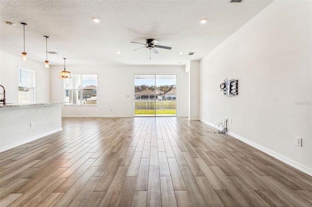 unfurnished living room with a ceiling fan, a textured ceiling, baseboards, and wood finished floors