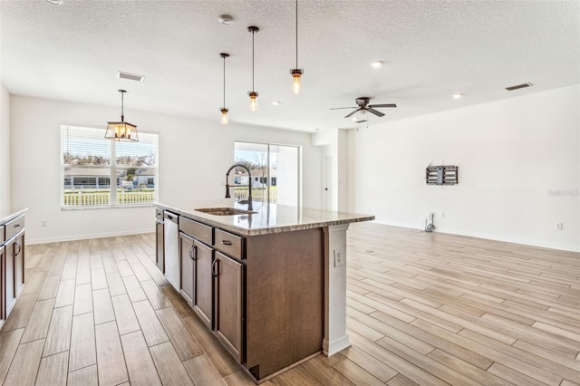 kitchen with visible vents, stainless steel dishwasher, wood tiled floor, open floor plan, and a sink