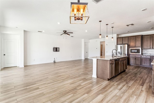 kitchen featuring built in microwave, open floor plan, a sink, light wood-type flooring, and stainless steel fridge with ice dispenser