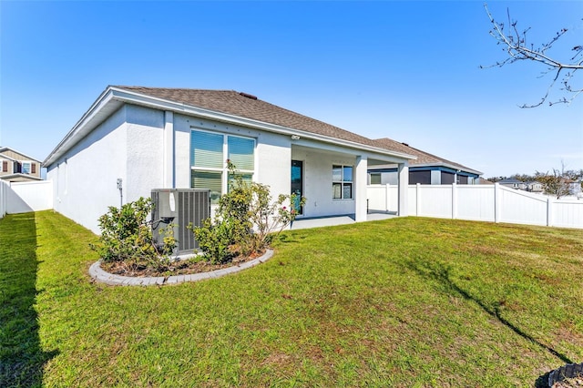 rear view of house with roof with shingles, a yard, stucco siding, central AC, and fence