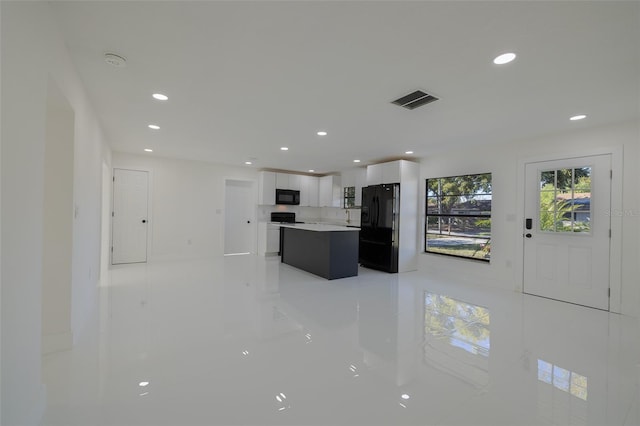 kitchen featuring visible vents, a center island, light countertops, black appliances, and white cabinetry