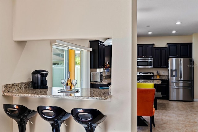 kitchen with stainless steel appliances, light stone counters, and dark cabinets