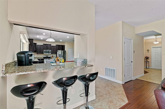 kitchen featuring a peninsula, visible vents, stainless steel appliances, and light stone counters