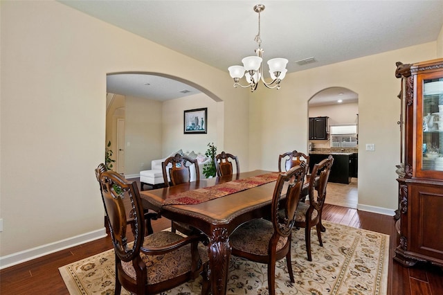 dining room featuring dark wood-type flooring, arched walkways, a chandelier, and visible vents