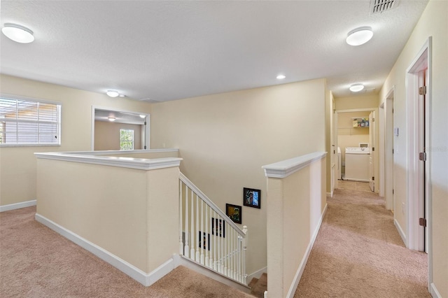 corridor with light carpet, washer / dryer, baseboards, visible vents, and an upstairs landing