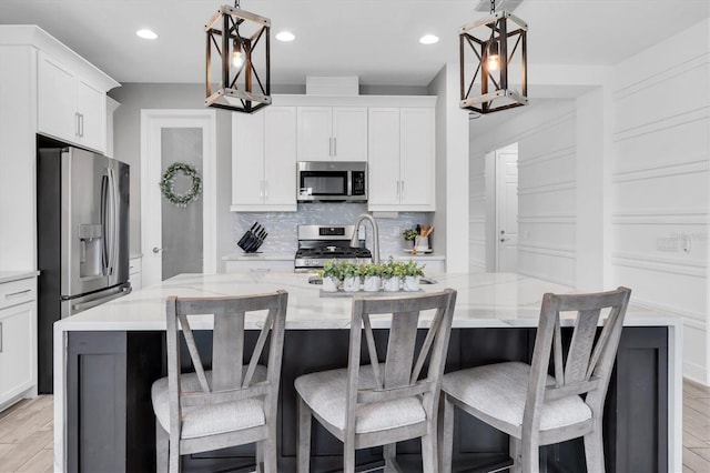 kitchen with a kitchen island with sink, stainless steel appliances, white cabinetry, light stone countertops, and tasteful backsplash