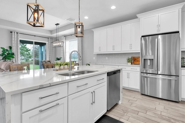 kitchen featuring a center island with sink, a sink, stainless steel appliances, light wood-type flooring, and backsplash