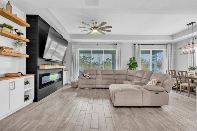 living room featuring light wood finished floors, ceiling fan with notable chandelier, visible vents, and a glass covered fireplace