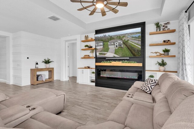 living room with visible vents, a tray ceiling, and a glass covered fireplace