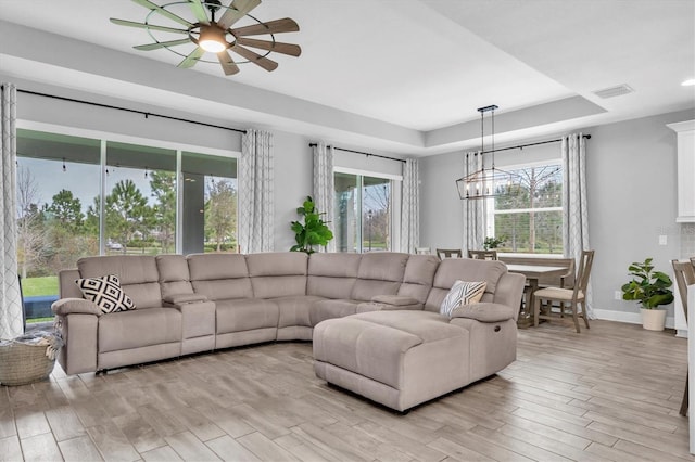 living room featuring light wood finished floors, baseboards, visible vents, ceiling fan, and a tray ceiling