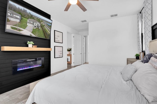 bedroom with a glass covered fireplace, visible vents, and wood finished floors