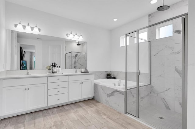 bathroom featuring wood finished floors, a sink, a marble finish shower, a bath, and double vanity