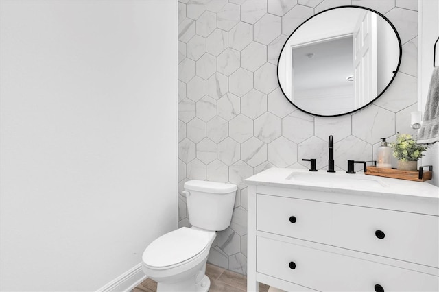 half bathroom featuring toilet, vanity, baseboards, tile walls, and tasteful backsplash