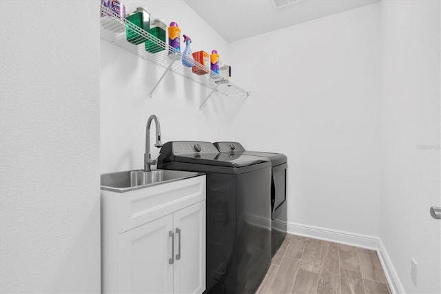 clothes washing area with light wood finished floors, cabinet space, washing machine and dryer, a sink, and baseboards