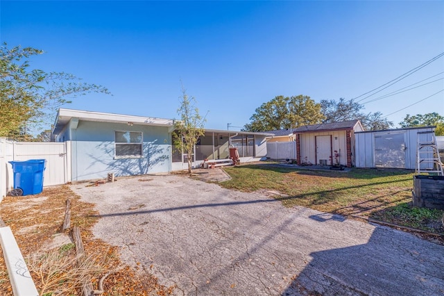 view of front of home featuring stucco siding, a storage unit, a front yard, fence, and an outdoor structure