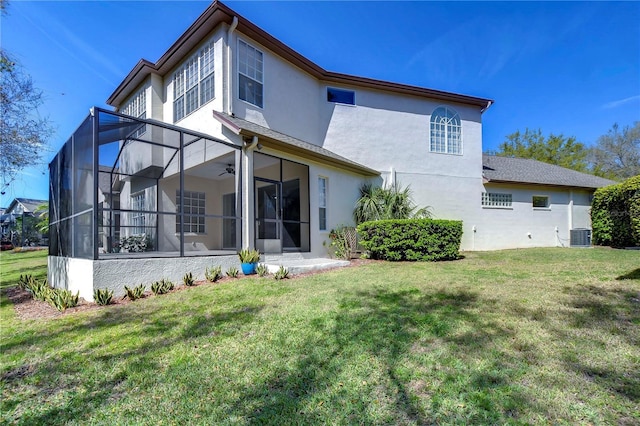 back of property with a ceiling fan, a lawn, central AC unit, and stucco siding