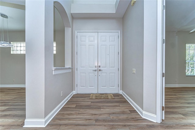 foyer with arched walkways, baseboards, and wood finished floors