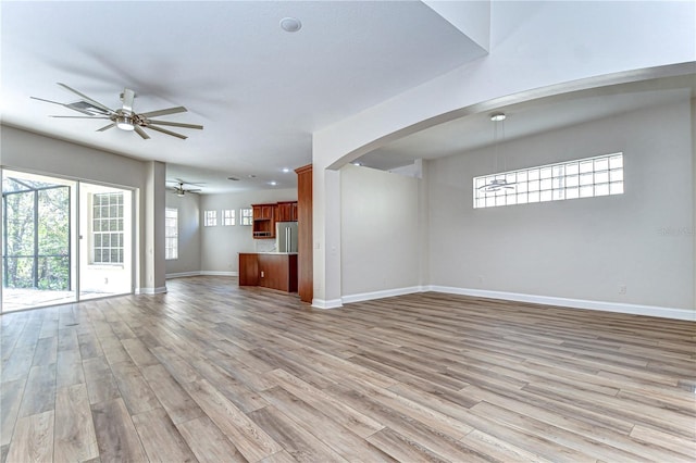 unfurnished living room featuring light wood-style flooring, baseboards, ceiling fan, and arched walkways