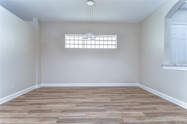 spare room with arched walkways, wood finished floors, and baseboards