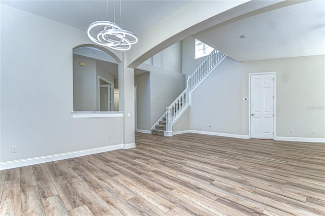 interior space featuring a high ceiling, wood finished floors, a chandelier, baseboards, and stairs