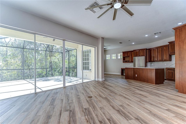 kitchen with a kitchen island, open floor plan, freestanding refrigerator, light countertops, and light wood-style floors