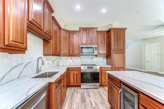 kitchen featuring beverage cooler, appliances with stainless steel finishes, light stone counters, light wood-style floors, and a sink